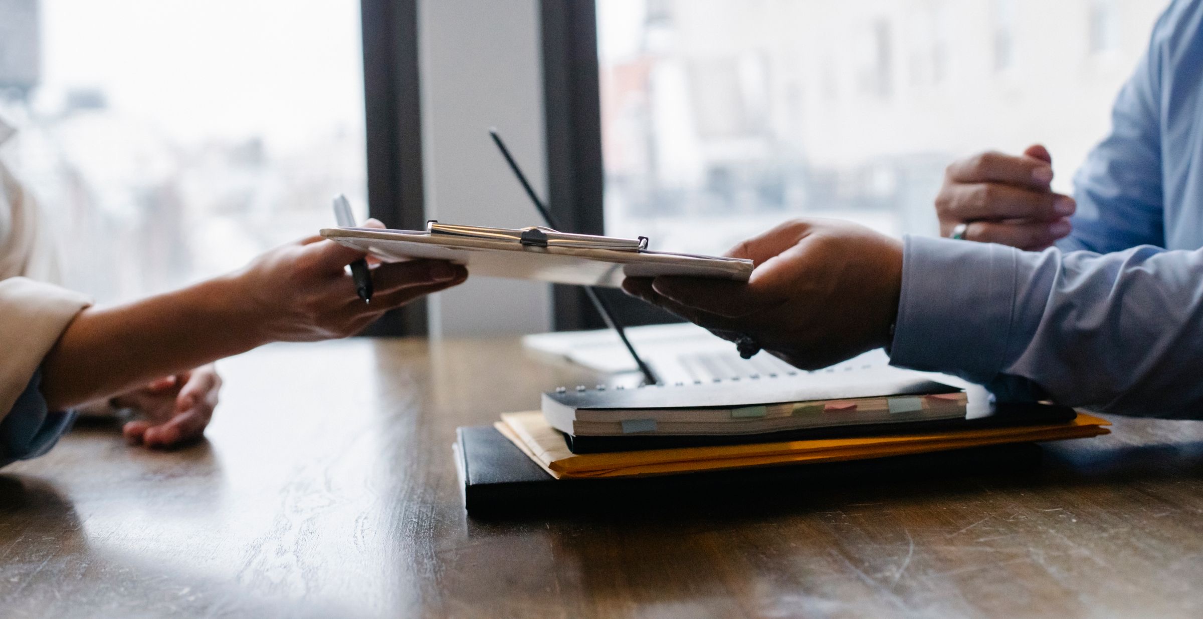 A hand passing a paper application form across a service counter to an office clerk