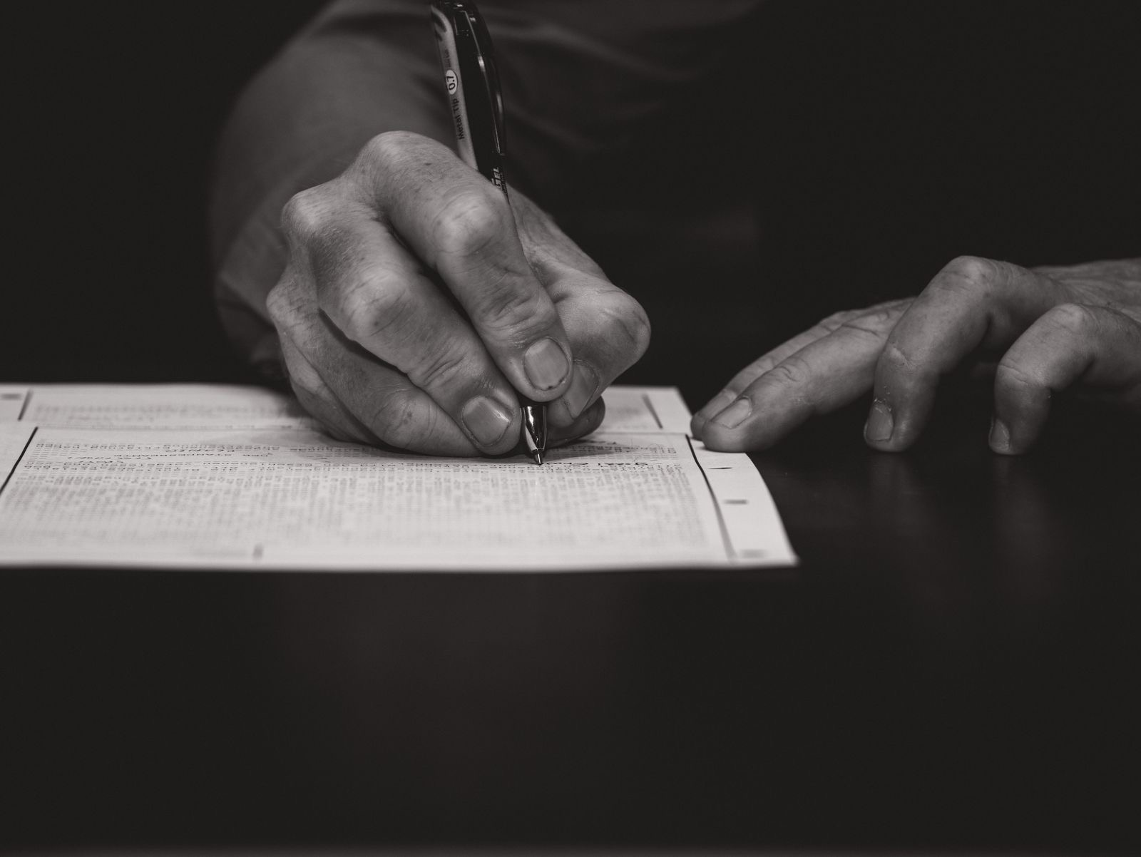 Hand filling in a paper form with a pen beside an envelope and stamps