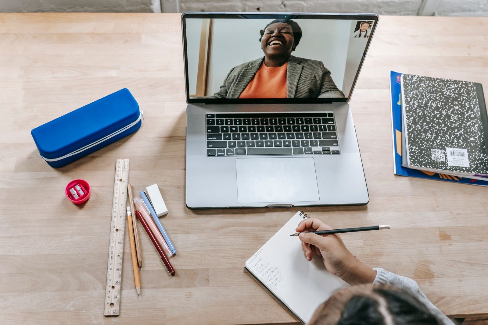 A laptop with a video call open beside a folder of papers on a desk